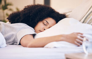 A peaceful woman with curly hair sleeping soundly on a comfortable bed, surrounded by soft pillows. The morning light gently illuminates the room, creating a calm and restful atmosphere.