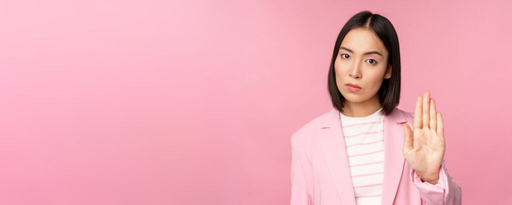 A woman with curly hair wearing a yellow cardigan joyfully spreading her arms outside, looking free and confident in an urban setting.