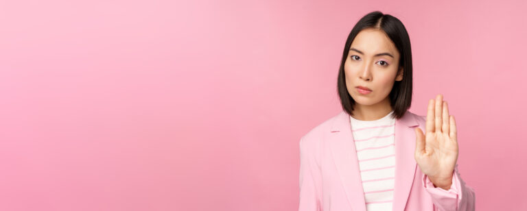 A woman with curly hair wearing a yellow cardigan joyfully spreading her arms outside, looking free and confident in an urban setting.