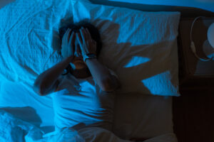 Woman lying awake at night with hands on her face, showing stress-related insomnia and nighttime anxietyWoman stretching gently in bed in the morning sunlight, representing natural wakefulness and circadian rhythm balance