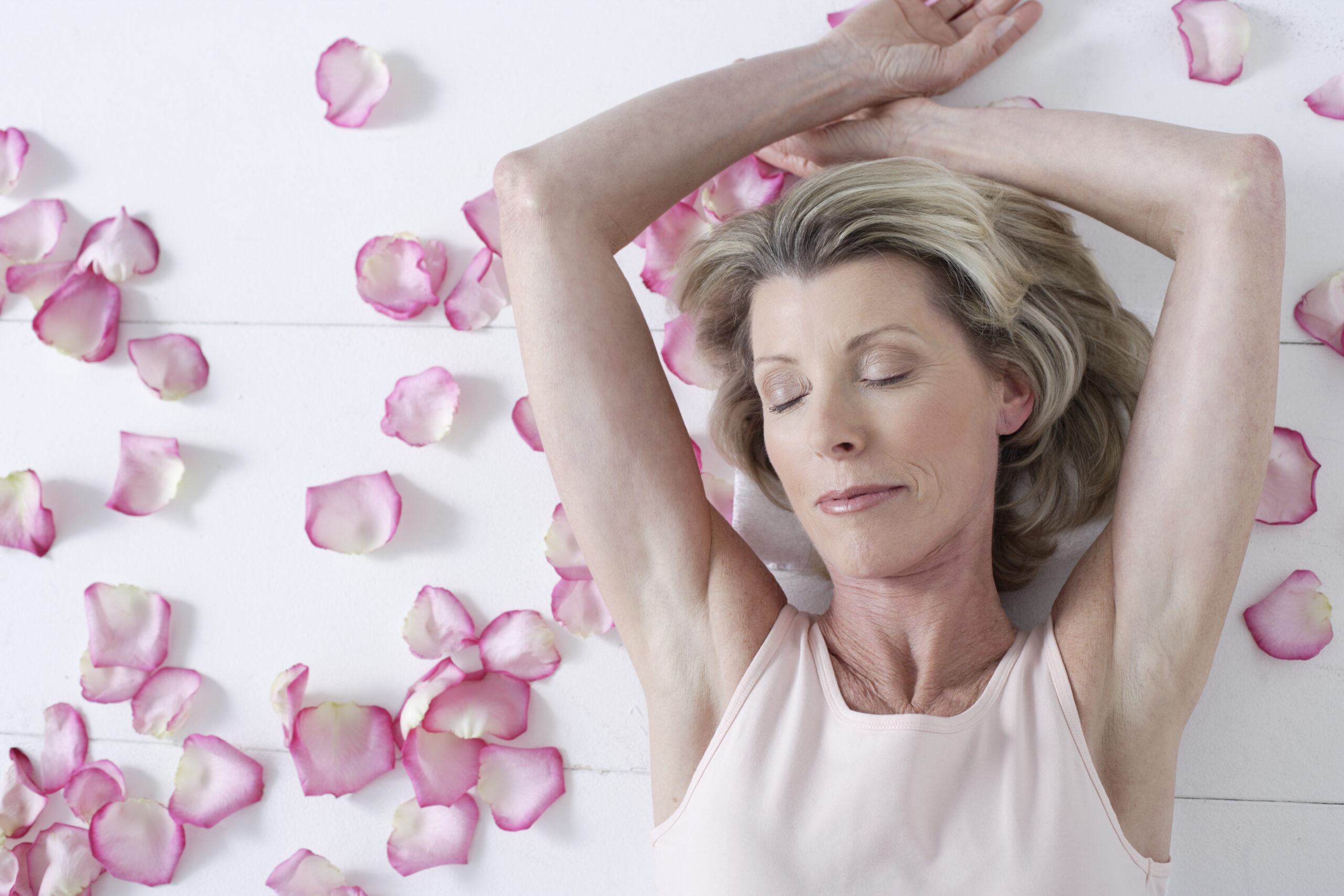 Confident midlife woman with eyes closed against a pink background, embracing change and inner calm.