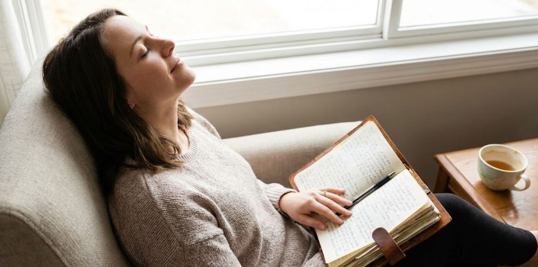 Close-up of a journal with handwritten journaling prompts for emotional release, accompanied by a cup of tea
