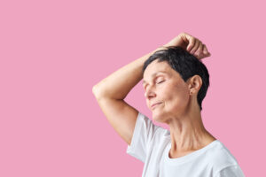 Confident midlife woman with eyes closed against a pink background, embracing change and inner calm.