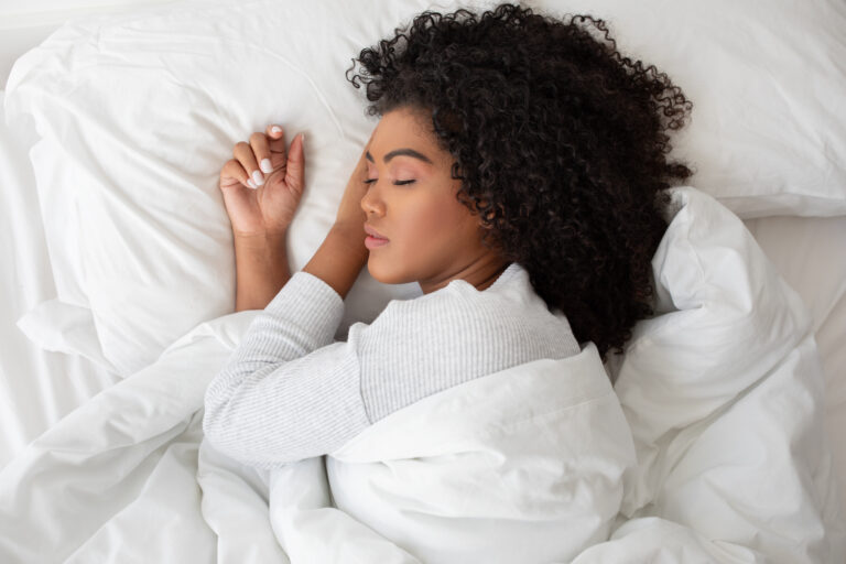 Young woman sleeping peacefully in white bedding, healthy deep sleep and nighttime relaxation